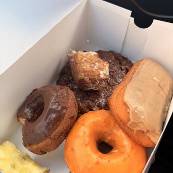 Assorted donuts including orange creme, apple fritter, maple bar, and a French cruller
