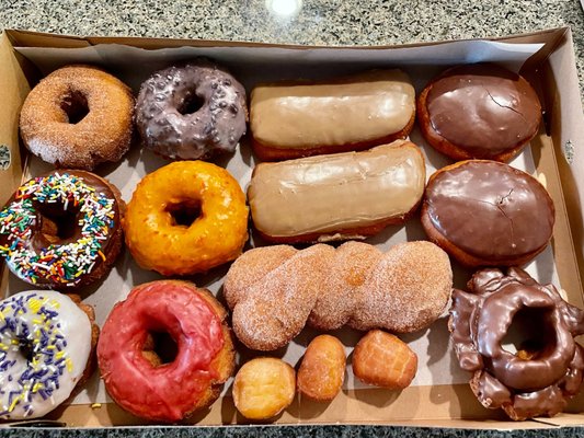 A dozen donuts in a pink bakery box, glazes and toppings varied